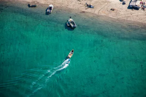 Arial view of a boat driving towards a beach. 