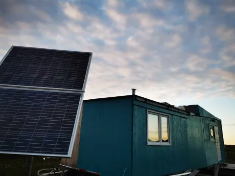 House at dusk with a solar panel in the foreground and illuminated windows in the background