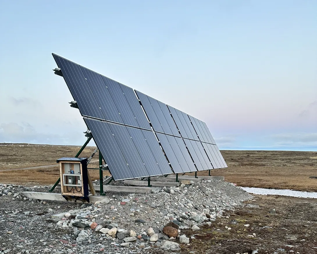 A row of solar panels during the spring/summer at dusk on the tundra. 